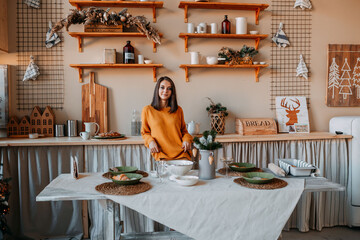 Happy woman in orange sweater in village house preparing for Christmas eve. Cooking dishes for new year eve. Scandinavian kitchen decorations. Bright kitchen with happy woman.