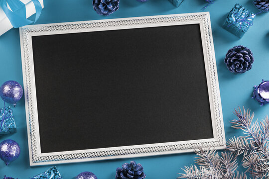 Photo frame with free black space around Christmas decorations and gifts on a blue background.