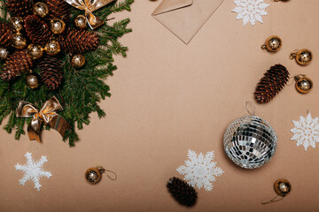 Christmas wreath decorations flat layout with space for text. Fir branches, pine cones, golden ornaments, disco ball and craft envelope on the cardboard background.