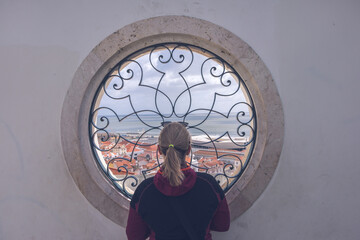 Woman is enjoying view from rounded window in historical center of Lisbon, Portugal.