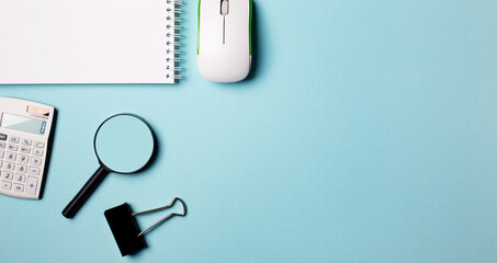 Notepad, magnifier, computer mouse and white wrist watch on a blue background. Place to insert text. Flat lay