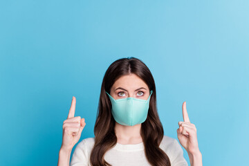 Photo of cute curly woman dressed white pullover face mask pointing up two fingers empty space isolated blue color background