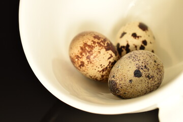 Obraz premium Three fresh quail eggs in a white bowl, close-up isolated on white.