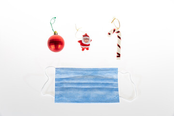 Christmas decoration on white background of candy cane, santa clause miniature, red ball and protective medical face mask for Covid-19.