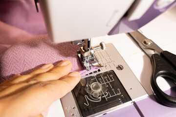 woman sews from purple fabric on a sewing machine close up