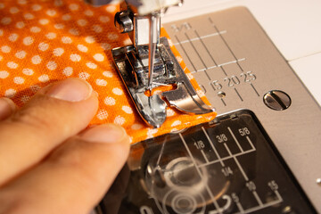 woman sews something from orange polka dot fabric  on a sewing machine