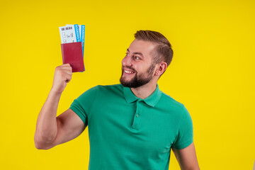 ortrait of a happy young man in sunglasses and green t-shirt holding passport isolated over yellow background