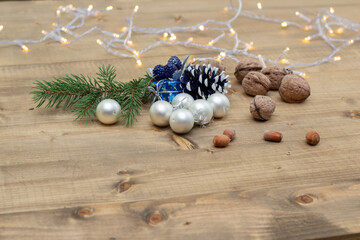 Fototapeta na wymiar Beautiful small silver and blue Christmas toys with a branch of a Christmas tree and nuts on a wooden background. Festive Christmas wooden background with lights. New Year's holidays.