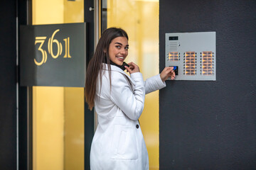Happy woman ringing on doorbell at building entrance. Using intercom. Young businesswoman on the...