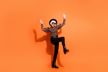 Fototapeta na wymiar Full size photo of old funky smiling cheerful positive lady in sunglasses dancing raise hands leg isolated on orange color background