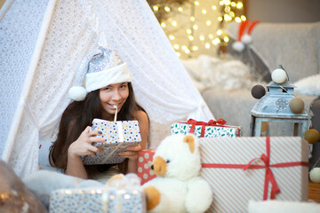 Pretty brunette woman wear silver color santa hat opens her christmas gift box with her teeth