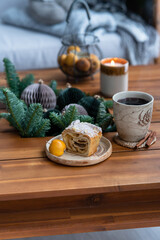 Close up of cake  and cup of tea with steam and candle on a coffee table. Breakfast over sofa in winter morning. Cozy holiday winter concept