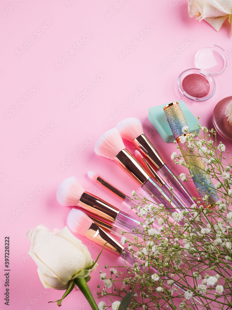 Wall mural shiny make up products and accessories on pink background with flowers. trendy holographic brushes.