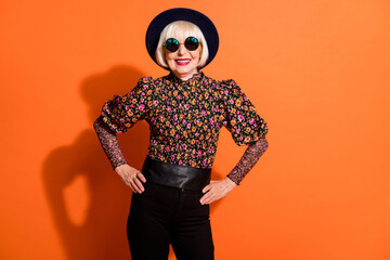 Photo of cheerful positive smiling toothy happy old woman wear sunglasses posing on camera isolated on orange color background