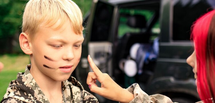 Young boy in camouflage with war paint on his face ready for laser tag shooting game. War simulation.	Banner.