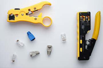 RJ45 twisted pair pair crimper on top and stripper with yellow handles on right and disassembled cable connectors in the center on white background. Composition from network tools.