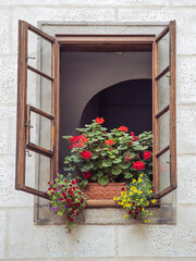 Fototapeta na wymiar An old wooden window has been opened in a stone European house. There are pots with red, yellow, purple flowers on the window. No people