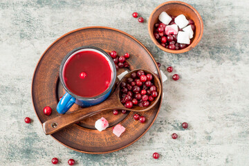 Blue mug with fruit drink on a brown ceramic platter, next to it a cup with lumps of sugar and fresh cranberries. A source of natural vitamins and minerals. Selective focus.
