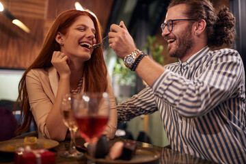 A young guy feeding his girlfriend at Valentine's day celebration at a restaurant. Together, anniversary, celebration