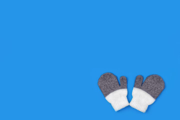 Wool knitted soft mittens half white, gray on top on a blue background. Warm winter clothing. Flat lay, top view