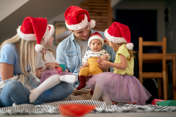 young family gathered for christmas, sitting on the floor at home, enjoying together. baby looking...