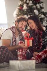 A young couple sitting on the floor enjoying Xmas presents. Christmas, relationship, love, together