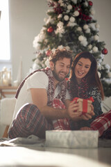A young excited couple in love sitting on the floor amazed by Xmas presents. Christmas, relationship, love, together
