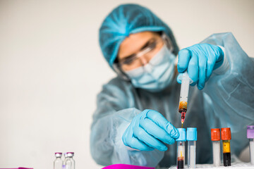 Blood test tube with label of Covid-19 also known as coronavirus or novel corona in scientist hand in laboratory. Female scientist is wearing highly protective suit, gloves, mask and glasses.