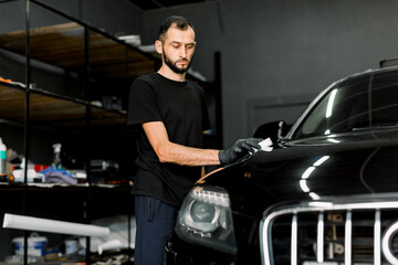 Young man, car polish service worker polishing car hood, buffing and polishing vehicle with nano...