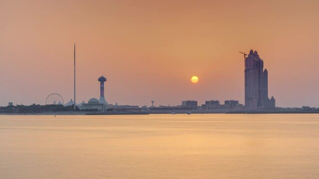 Sunset in Abu Dhabi over Marina Island timelapse, view from corniche. Orange warm light and reflection on water. Construction site with crane