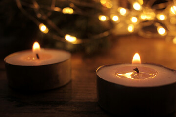 Christmas candles on dark background. Festive tea candlelight and blurred garland light
