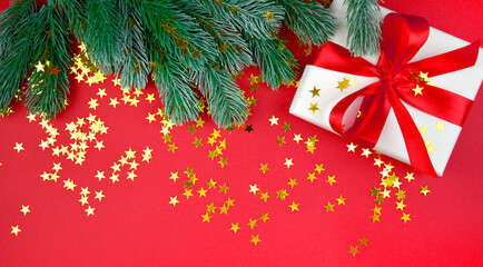 Holiday mock up composition with gift box, fir tree branch and confetti on red background. Greeting cad for Christmas and New year. Border. Copyspace.