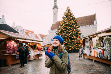 Tallinn, Estonia. Young Beautiful Pretty Caucasian Girl Woman Dressed In Green Jacket And Blue Hat Enjoying Life And Smiling On Background Christmas Xmas New Year Market