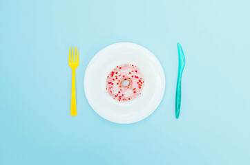 Pink donut on a blue plate with cutlery.