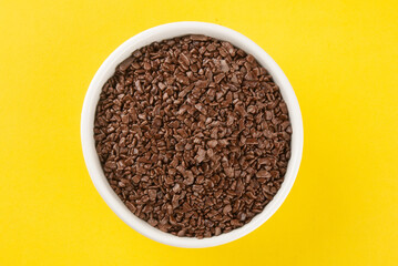Granulated chocolate in white bowl with yellow background.