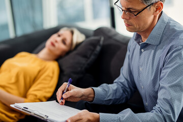 Mental health professional taking notes while having therapy session with a patient.