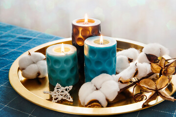 Fototapeta na wymiar Christmas composition in blue and gold. Burning candles and a cotton branch on a gold tray. Bokeh background.