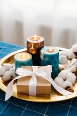 Christmas composition in blue and gold. Gift box, burning candles and box of cotton on gold tray.