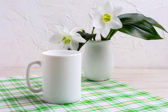 White coffee mug mockup with lily in vase on green checkered napkin