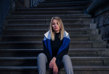Urban Portrait of a young woman, looking at the camera, with serious expression, sitting in a staircase in the city.