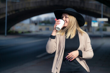 Portrait of a young woman, wearing casual clothing, and a hat, drinking a coffee, in the city.