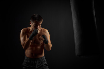 Obraz na płótnie Canvas Male boxer punching in boxing bag on black background