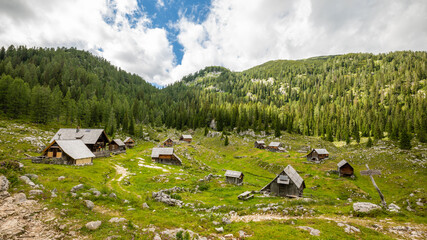 Lovely wooden cottages stand near a pine forest covered mountain in the tranquil Julian Alps en route to the Triglav Seven Lakes, Triglav National Park, Slovenia.