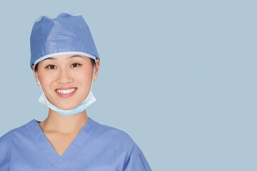 Close-up portrait of female surgeon smiling over light blue background