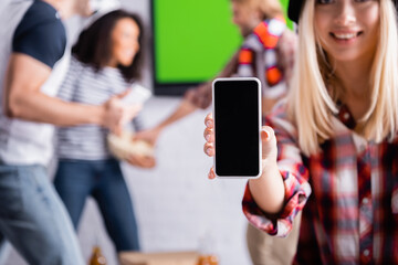 smiling woman showing smartphone with blank screen near multiethnic sports fans on blurred background