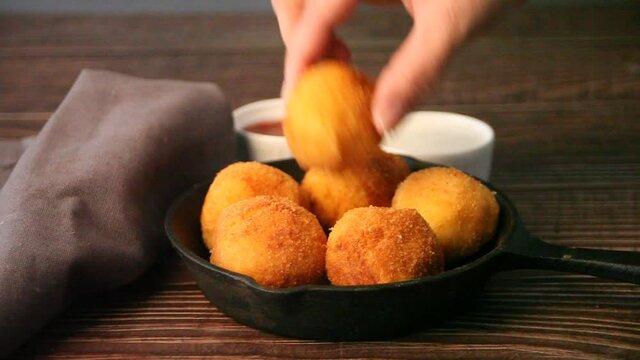 Woman hand take a one potato croquettes balls and dip in sauce