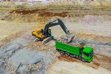 quarrying clay. yellow bulldozer mines clay and loads into green truck. Clay mining process.