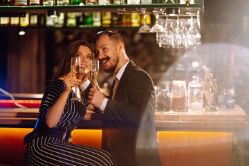 Happy loving couple enjoying having drinks together at the bar. Young man and woman clinking a glass champagne, enjoying winter holiday. Party, celebration, drink, birthday concept. Romantic evening.