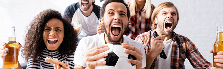 excited multiethnic friends screaming while watching football championship at home, banner