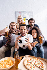 Fototapeta excited multiethnic football fans screaming while watching championship near beer, pizza and chips obraz